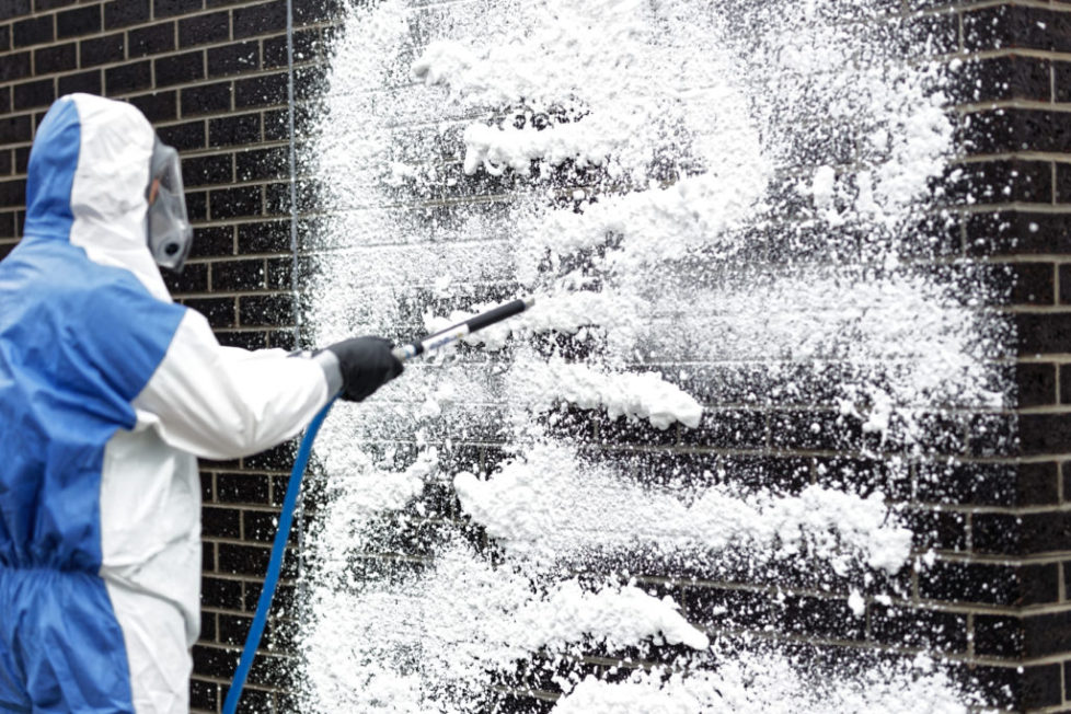 White Spray Foam on Brown Brick Wall by Man in Blue Coveralls